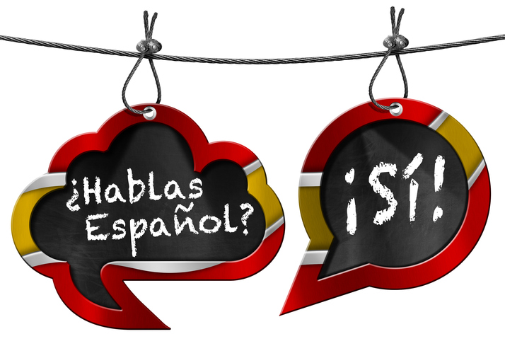 Two speech bubbles with Spanish flag and text Hablas Espanol? Si! Hanging from a steel cable and isolated on white